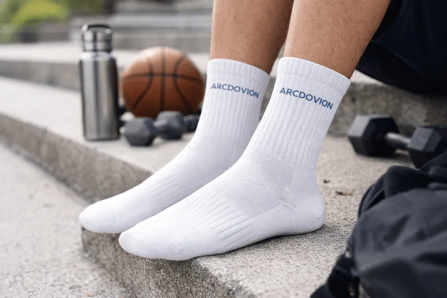 White ARCDOVION crew socks worn outdoors beside a basketball and training bag